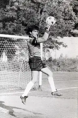 A black-and-white photo of Mirsad Jonuz in the air, holding a ball up in front of a soccer goal.
