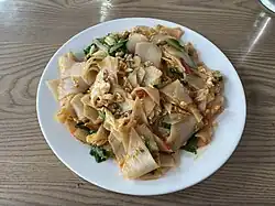 Image of da jiu-jia on a plate. Consists of thinly sliced, square rice cakes with small pieces of egg, peppers and spinach.