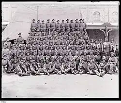 Eight rows of men in uniform with slouch hats in front of a building