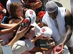 African American male in stocking cap signs autographs for fans on footballs
