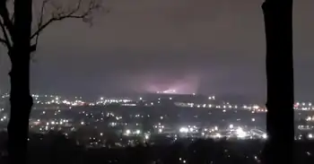 A partly-visible tornado illuminated by a bright flash between two trees