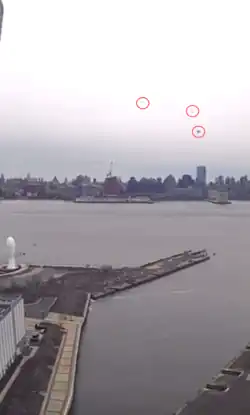 A CCTV still of the helicopter broken into three pieces, with Jersey City's Newport Pier in the foreground, Manhattan's Pier 40 in the background