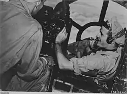 A black and white photograph of two men seated and working in the front cabin of an aircraft