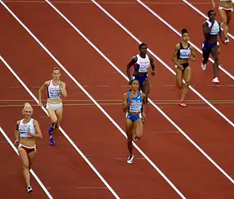 Photo of seven athletes running on a red track with white lane stripes