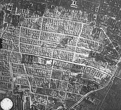 An aerial photograph of the former Warsaw Ghetto area, showing the camp's structure (a long and narrow rectangle in the image's centre) surrounded by Warsaw Ghetto's ruins