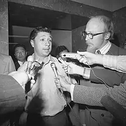 Man talks into several microphones held by reporters.