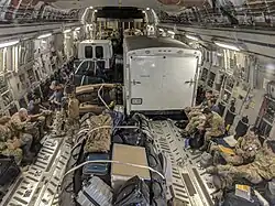 Photograph of the inside of a cargo jet, containing people in military field uniforms, equipment, and trucks (from Tropical cyclone response)