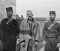 Schinas is standing between two armed guards