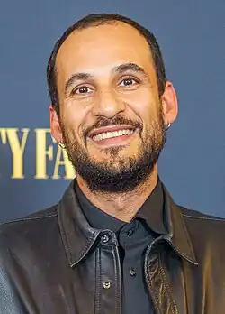 close-up of Ali Abbasi wearing a black shirt and black leather jacket, grinning directly at camera