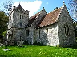 A short flint church with a red tiled roof, and a battlemented south tower with a pyramidal roof