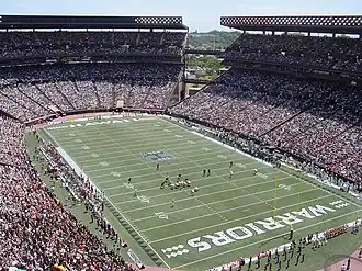 A football field with players lined up in the middle of it surrounded by a packed stadium