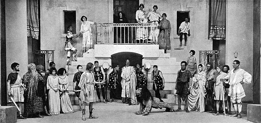 Scene in Ancient Roman arena with slender man in tunic and a lion, centre, with the Emperor and other Romans looking on