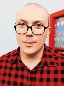 A man with black eyeglasses and a red flannel shirt in a room with albums displayed in the background