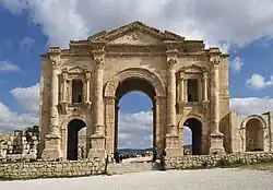 Looking North, a large stone arch can be seen, bathed by the light of the sun on the golden stone. It has many decorative features, and a smaller arch on each side of the central one.