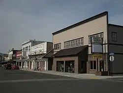 A small, two-story building with a sign for "Arlington Hardware & Lumber" facing a city street, joined by similar-sized buildings with business of their own.