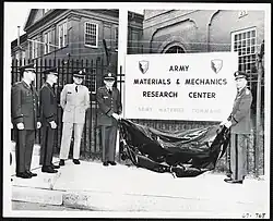 Army officials at Watertown Arsenal unveil a new sign that reads “Army Materials & Mechanics Research Center” in a large dark font and “Army Materiel Command” underneath in a smaller, lighter font.