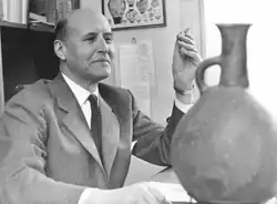 Furumark, a bald man in middle age wearing a formal suit, sat at his desk studying a Mycenaean vase.