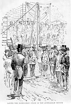 Black and white print showing a crowd of men in top hats. A caption reads "Laying the foundation stone of the Australian Church".