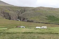 A farm building amid an expanse of grass. There are hills rising in the background.