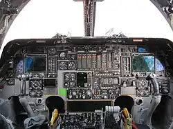 A flightdeck, dominated by a mix of new and analogue instruments. On both sides are control yokes. Light enters through the forward windows
