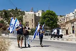 A woman and 2 flag bearing young men walking in a street in Hebron