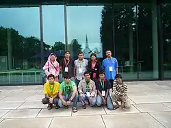 Ten people facing forward, in two lines of five. In the front row are five boys in their late teens. Behind them are four adults, and one person who appears to be in his late teens.