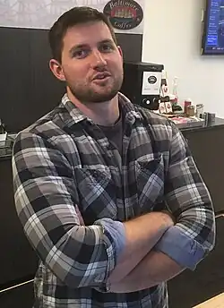 A man in Lumbersexual style, 2016, wearing a flannel shirt and groomed beard, blending rugged Americana with hipster grooming trends.
