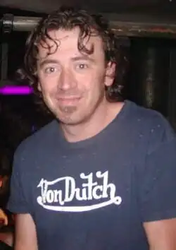 A man with short brown hair wearing a blue T-shirt with "Von Dutch" written on it