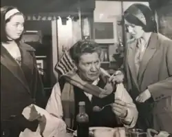 Still from the film showing Alfie Bass a Bindle seated at a table eating, with (standing) his wife on his left and his daughter on the right.