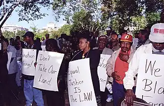 Black farmers protest at Lafayette Park across from the White House in Washington, D.C. on September 22, 1997. Protesters are holding-up signs labeled with phrases. "Don't take our land", "Equal Justice is the Law", and more but they are cute off.