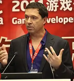 An image of Brian Fargo. He is standing behind a podium.