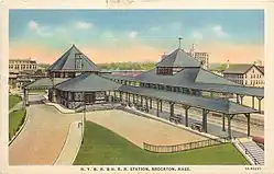 A postcard showing two stone railway stations flanking elevated tracks in a city