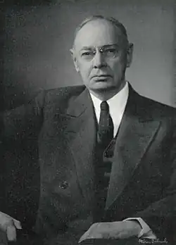 Formal black and white portrait of an aged Brown, wearing glasses, in a suit