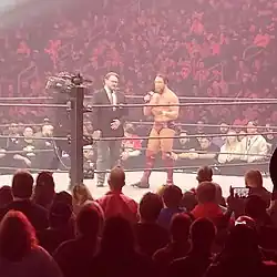 A color photograph of two men and a cameraman in a professional wrestling ring