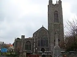 A flint church seen from the west, showing from the right, the tower and the west ends of the nave and the north aisle
