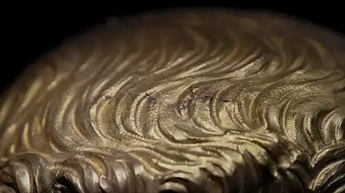 Small gray wave-shaped marks on a gold surface.