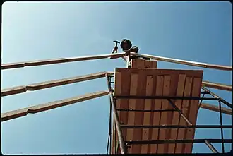 Pipe staging is very common in the U.S. Welded sections stack on top of each other and braced with cross braces, workers stand on planks or aluminum platforms, 1975.