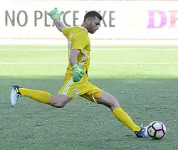 A soccer goalkeeper in a yellow jersey kicks a soccer ball.