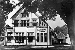 A triangular shaped building with many windows with its view slightly obscured by a massive tree