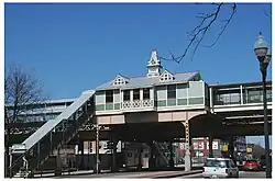 A green station house in a Queen Anne style, with a staircase on the left side leading up to it.