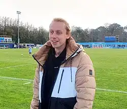 Man in a warm coat standing on a football pitch looking in front of him.