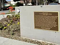 Blossoming aloe plants beside brown and gold commemorative plaque on low wall