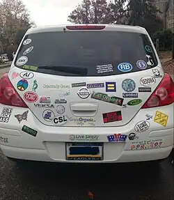 The rear of a Nissan Versa displaying many bumper stickers.