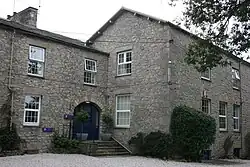Large grey stone two-story building with a short staircase up to a blue entrance door,