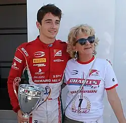 Leclerc holds his trophy after winning the FIA Formula 2 Championship, with his arm around his mother