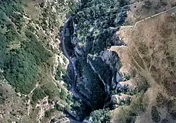 Looking down into the gorge with a road with cars on it running from the top to the bottom of the picture. To the left are less steep slopes covered in vegetation.