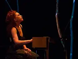 Christine Ott wearing a dark sleeveless top, appearing to play a keyboard instrument onstage while looking upward