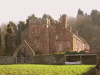 Red brick building with tall chimneys. In the foreground is an arched gateway.
