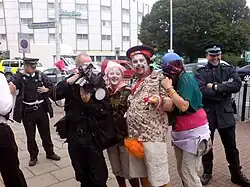 Three protesters dressed as clowns posing with a FIT photographer. Other officers are stood around smiling