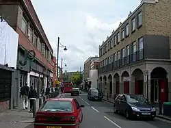 Photograph of a busy street with cars and pedestrians, with buildings on both sides